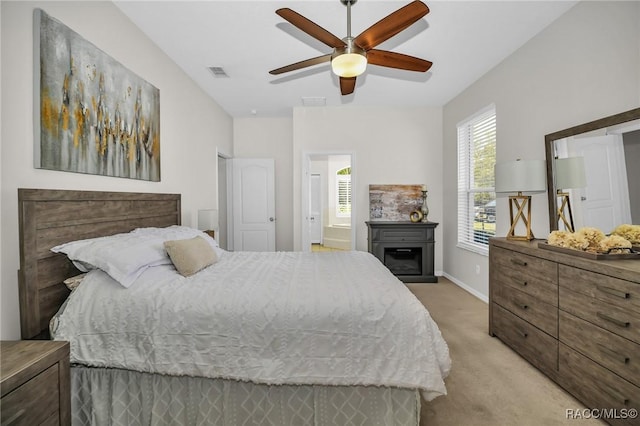 bedroom featuring visible vents, ensuite bathroom, a glass covered fireplace, baseboards, and light colored carpet