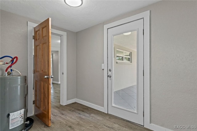 1 Taft St, Beverly Hills, FL 34465 - doorway to outside with water heater, light wood-type flooring, baseboards, a textured wall, and a textured ceiling