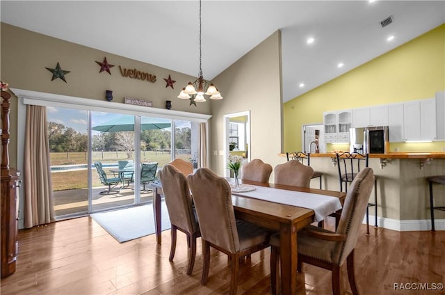 dining space featuring hardwood / wood-style flooring, a chandelier, and high vaulted ceiling