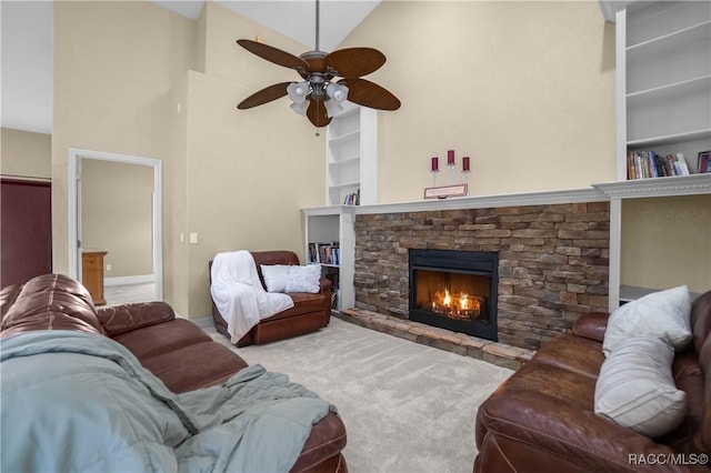 carpeted living room with built in shelves, ceiling fan, a stone fireplace, and vaulted ceiling