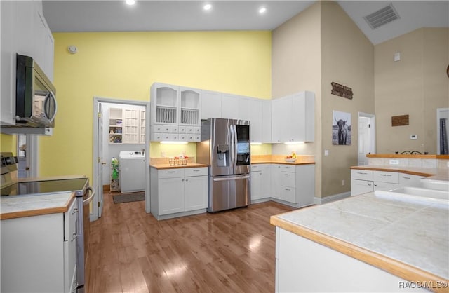 kitchen featuring high vaulted ceiling, washer / dryer, white cabinets, stainless steel appliances, and light hardwood / wood-style flooring