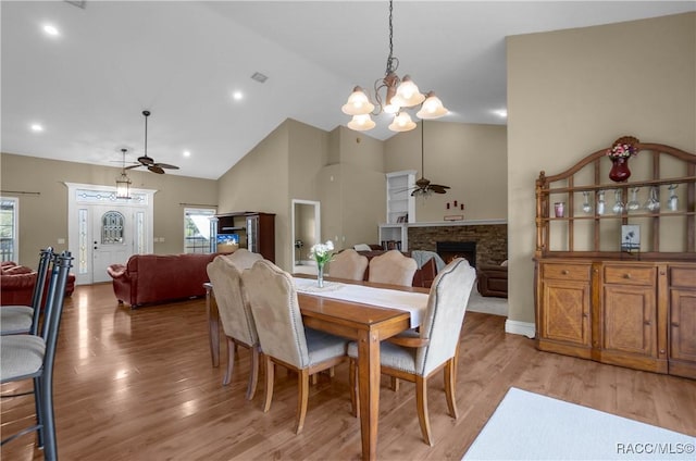 dining room featuring high vaulted ceiling, a fireplace, ceiling fan with notable chandelier, and light hardwood / wood-style flooring