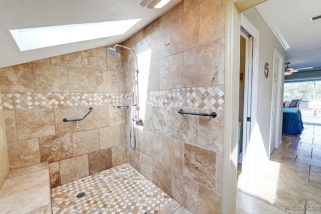 bathroom with ornamental molding, vaulted ceiling with skylight, a textured ceiling, ceiling fan, and tiled shower