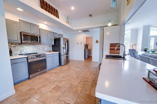 kitchen featuring sink, backsplash, crown molding, gray cabinets, and appliances with stainless steel finishes