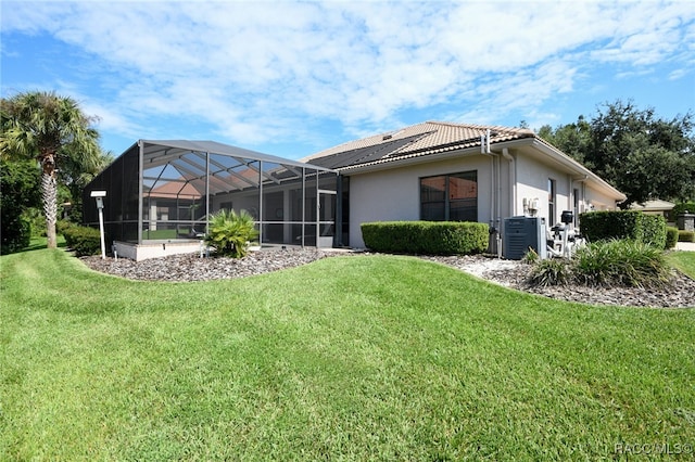 back of house featuring glass enclosure, central AC unit, and a lawn