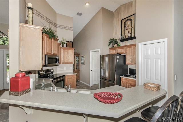 kitchen featuring high vaulted ceiling, a kitchen breakfast bar, kitchen peninsula, and appliances with stainless steel finishes