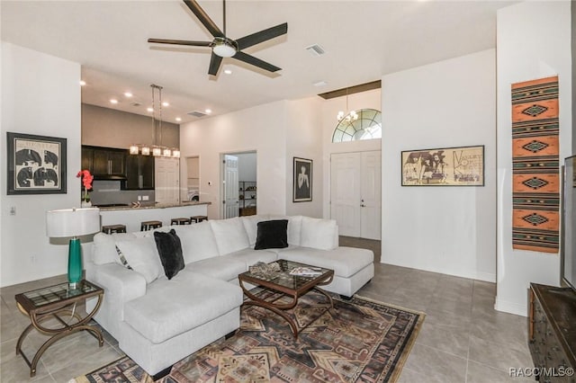 living room featuring ceiling fan with notable chandelier, light tile patterned flooring, and a towering ceiling