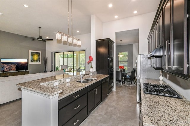 kitchen with light stone countertops, sink, hanging light fixtures, a kitchen island with sink, and appliances with stainless steel finishes