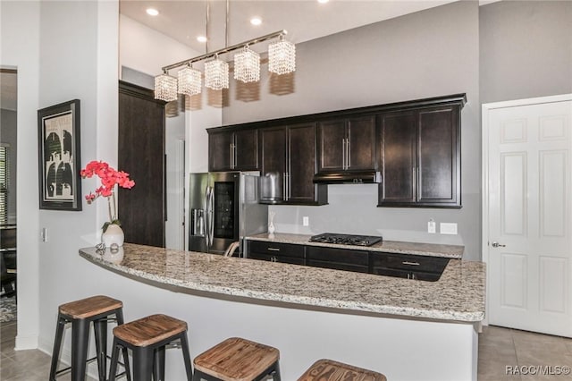 kitchen featuring kitchen peninsula, stainless steel fridge, light stone countertops, and hanging light fixtures