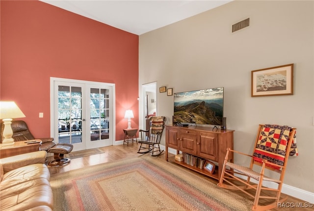 living area featuring french doors, a towering ceiling, and hardwood / wood-style floors