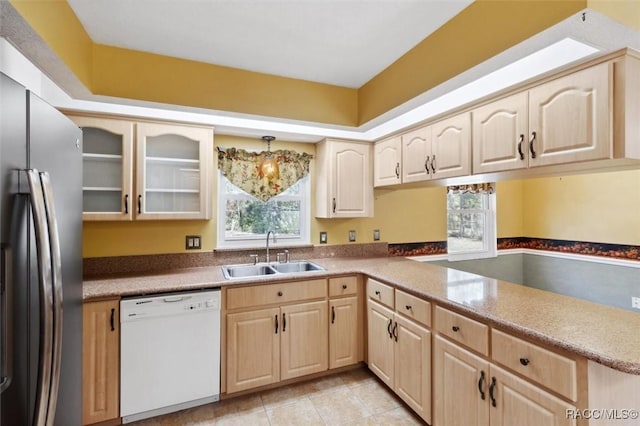 kitchen featuring white dishwasher, a sink, stainless steel refrigerator with ice dispenser, light brown cabinetry, and glass insert cabinets