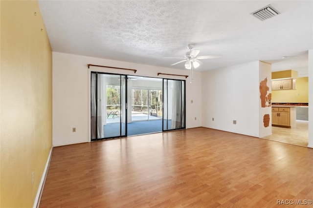 unfurnished room with light wood-type flooring, a ceiling fan, visible vents, and a textured ceiling