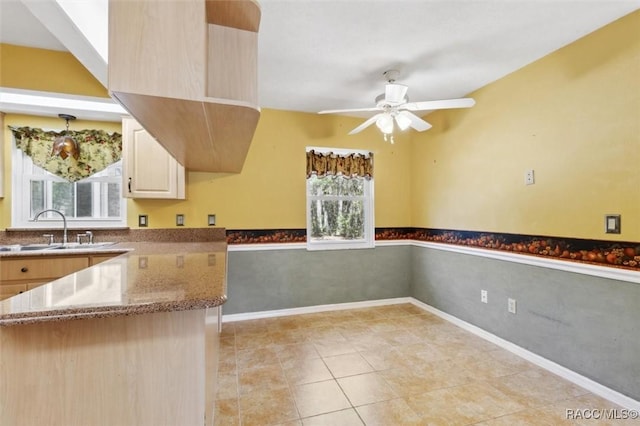 kitchen featuring a wainscoted wall, ceiling fan, light stone counters, and a sink