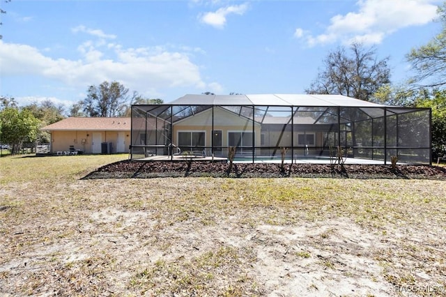 back of property with glass enclosure, an outdoor pool, and a lawn