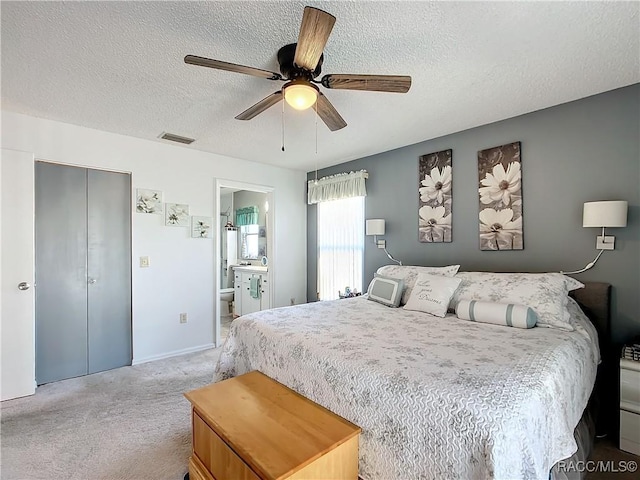 bedroom featuring ensuite bathroom, ceiling fan, light carpet, a textured ceiling, and a closet