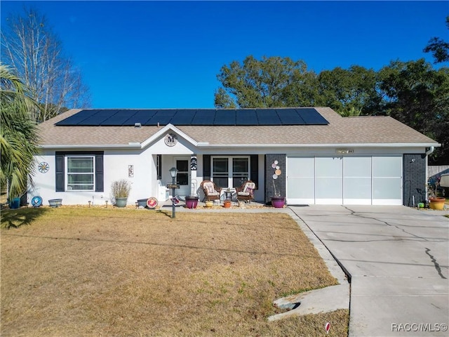 single story home featuring a garage, solar panels, covered porch, and a front lawn