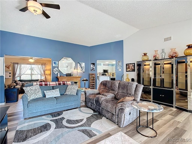 living room with ceiling fan, lofted ceiling, a textured ceiling, and light hardwood / wood-style floors