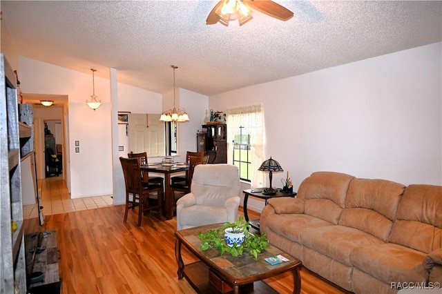 living room featuring ceiling fan with notable chandelier, vaulted ceiling, a textured ceiling, and hardwood / wood-style flooring