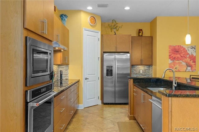 kitchen with appliances with stainless steel finishes, tasteful backsplash, sink, decorative light fixtures, and dark stone countertops