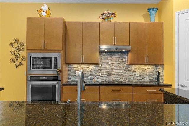 kitchen with dark stone countertops, appliances with stainless steel finishes, and backsplash