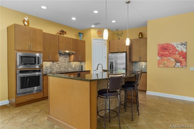 kitchen with hanging light fixtures, appliances with stainless steel finishes, tasteful backsplash, an island with sink, and a breakfast bar area