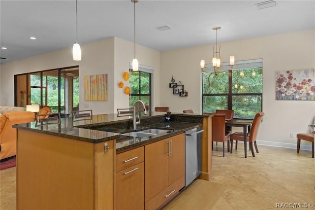 kitchen featuring a center island with sink, dishwasher, hanging light fixtures, and dark stone countertops