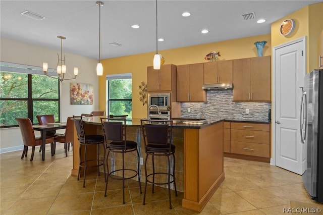 kitchen featuring hanging light fixtures, tasteful backsplash, a wealth of natural light, a center island with sink, and stainless steel appliances