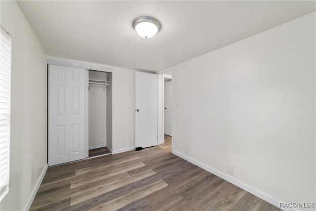 unfurnished bedroom with a closet, dark wood-style floors, and baseboards