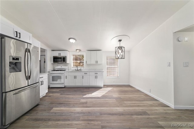 kitchen with appliances with stainless steel finishes, decorative light fixtures, white cabinets, light countertops, and wood finished floors