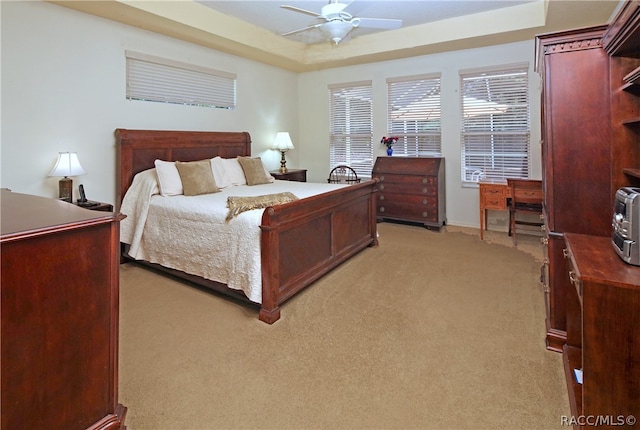 bedroom with light carpet, a raised ceiling, and ceiling fan