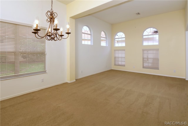 carpeted spare room featuring plenty of natural light and a notable chandelier