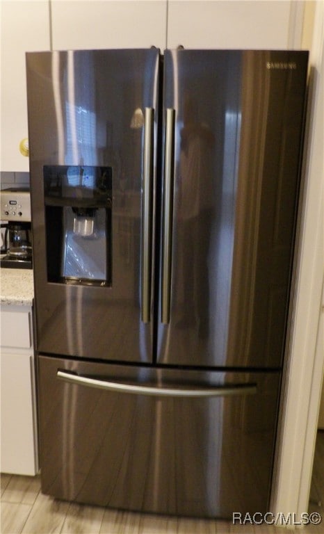 interior details featuring stainless steel fridge, white cabinetry, and light stone counters