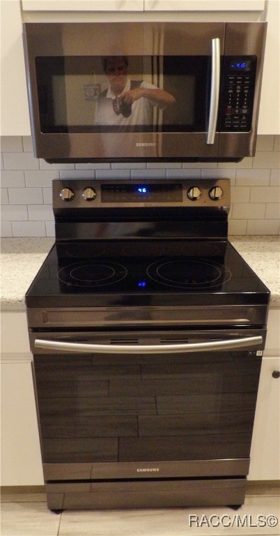 details featuring white cabinets, light stone countertops, stainless steel appliances, and tasteful backsplash