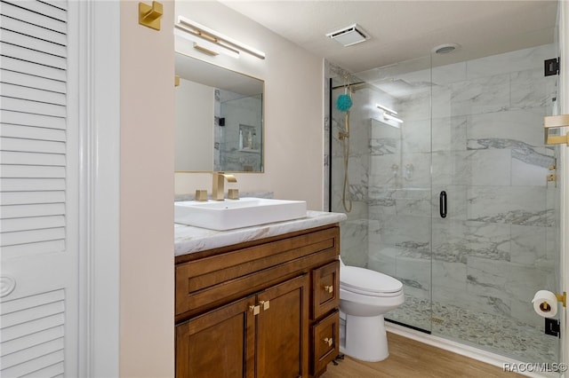 bathroom with hardwood / wood-style floors, vanity, a shower with door, and toilet