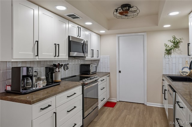 kitchen featuring decorative backsplash, appliances with stainless steel finishes, light wood-type flooring, sink, and white cabinetry