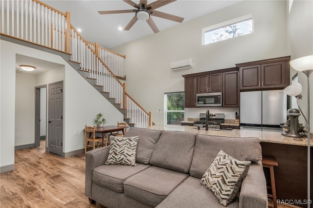 living room with light hardwood / wood-style floors, an AC wall unit, ceiling fan, and a high ceiling