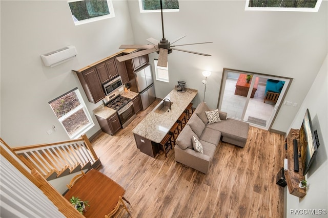 living room with sink, ceiling fan, a towering ceiling, a wall mounted air conditioner, and light hardwood / wood-style floors