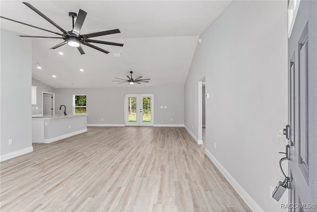 unfurnished living room featuring ceiling fan, french doors, sink, light hardwood / wood-style flooring, and lofted ceiling