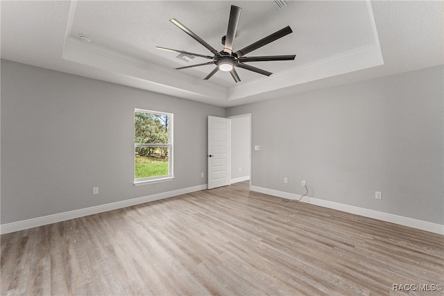 spare room with a tray ceiling, ceiling fan, and light wood-type flooring