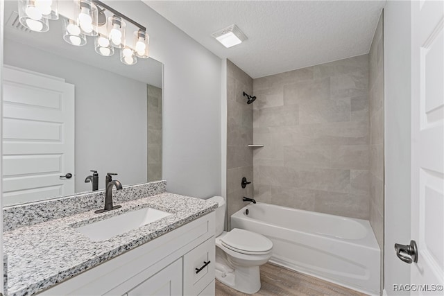 full bathroom with hardwood / wood-style floors, vanity, tiled shower / bath combo, toilet, and a textured ceiling