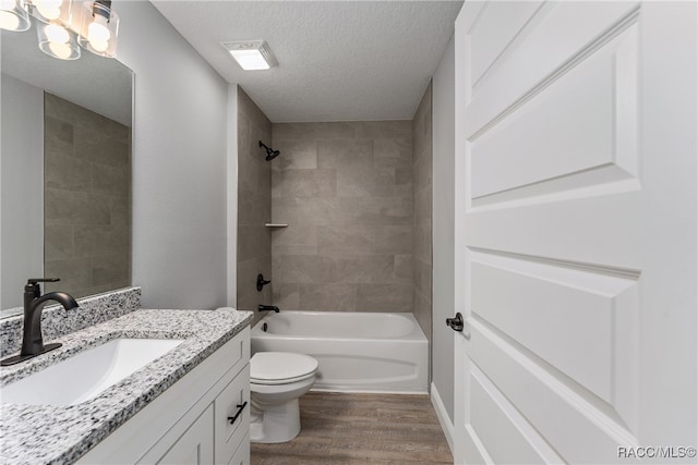 full bathroom featuring hardwood / wood-style floors, vanity, tiled shower / bath, toilet, and a textured ceiling