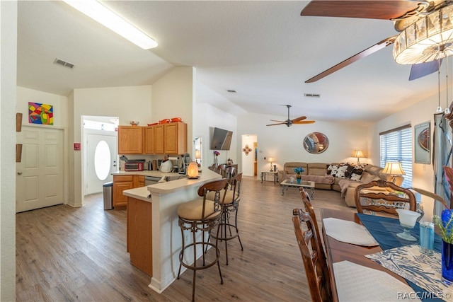 kitchen featuring kitchen peninsula, light wood-type flooring, ceiling fan, a breakfast bar area, and lofted ceiling