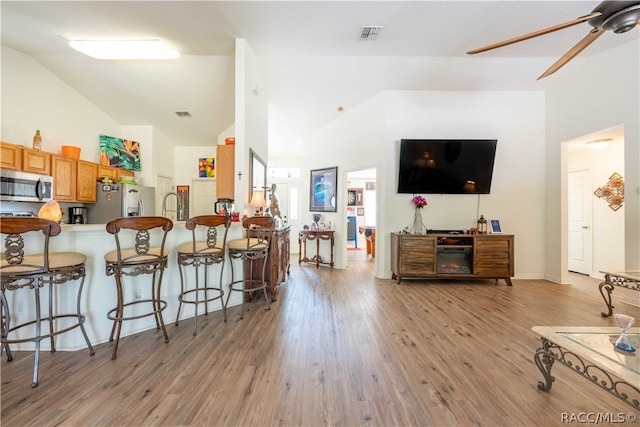 living room featuring ceiling fan, light hardwood / wood-style floors, sink, and high vaulted ceiling