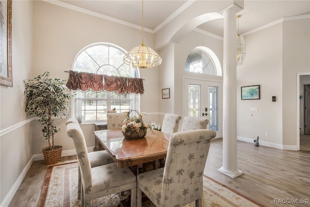 dining area with decorative columns, crown molding, hardwood / wood-style flooring, an inviting chandelier, and a high ceiling