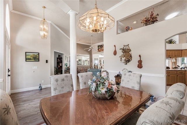 dining space with a high ceiling, ceiling fan with notable chandelier, ornamental molding, and hardwood / wood-style floors