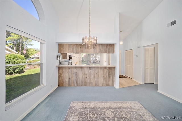 kitchen featuring high vaulted ceiling, a notable chandelier, kitchen peninsula, carpet floors, and decorative light fixtures