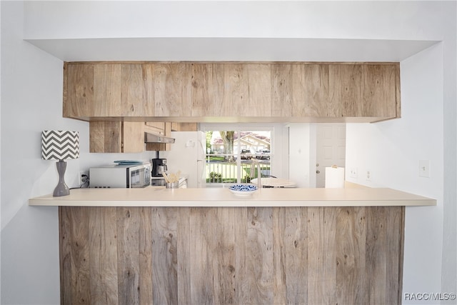 kitchen with kitchen peninsula, light brown cabinetry, and white fridge