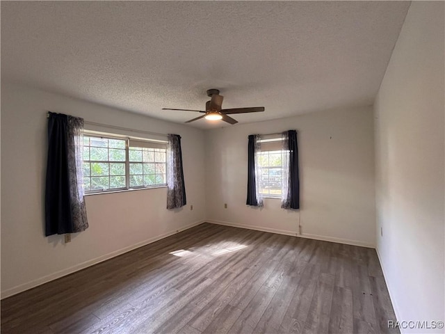 spare room with a textured ceiling, dark wood-style flooring, a wealth of natural light, and baseboards