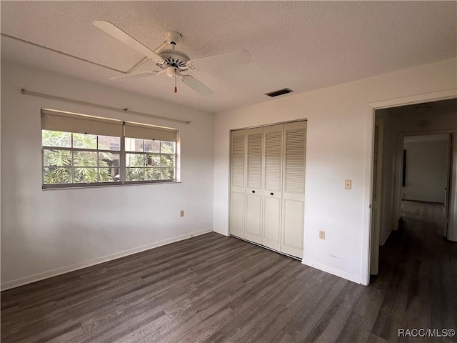 unfurnished bedroom with a textured ceiling, dark wood-style flooring, a closet, and visible vents