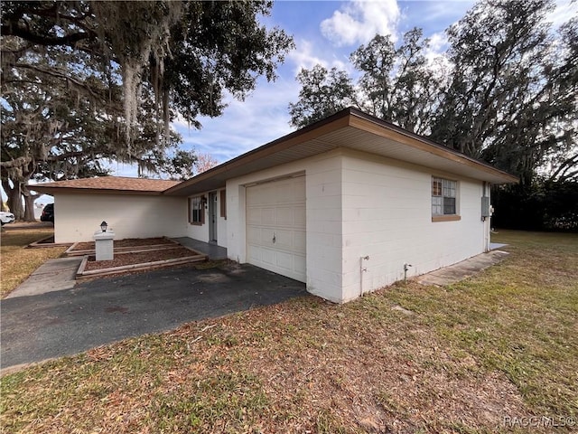 view of home's exterior with a garage, concrete block siding, a yard, and driveway